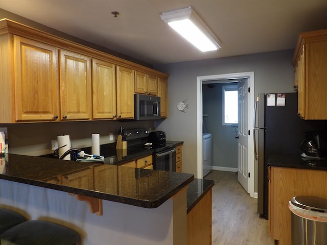 kitchen with stainless steel appliances, a kitchen breakfast bar, kitchen peninsula, dark stone counters, and light hardwood / wood-style floors