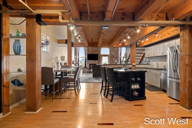 dining area with a fireplace, beam ceiling, light wood-type flooring, and wooden ceiling