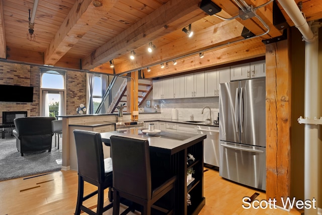 kitchen with kitchen peninsula, appliances with stainless steel finishes, a kitchen bar, sink, and light hardwood / wood-style flooring