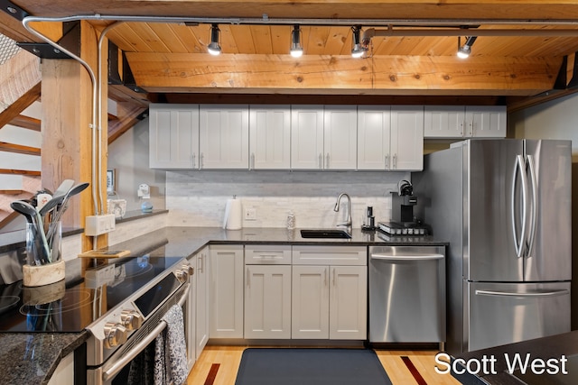 kitchen with track lighting, sink, appliances with stainless steel finishes, and dark stone counters