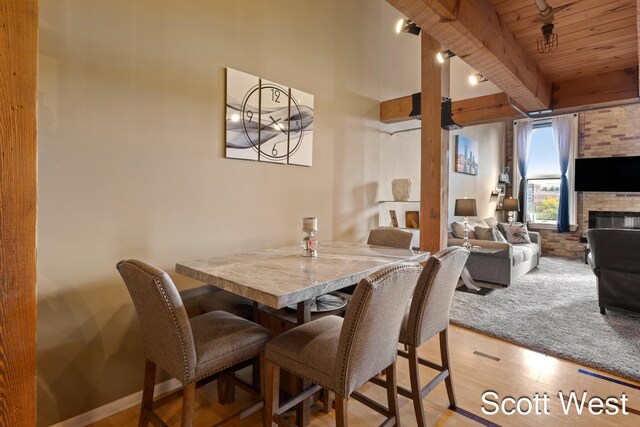 dining space featuring a large fireplace, light hardwood / wood-style flooring, wooden ceiling, and beam ceiling