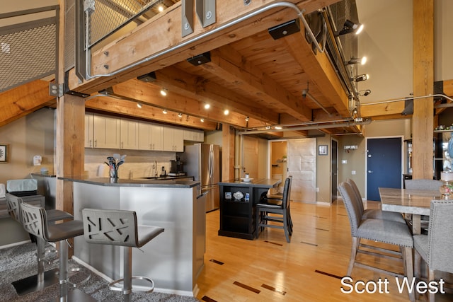 kitchen featuring a kitchen bar, light wood-type flooring, beam ceiling, white cabinetry, and stainless steel refrigerator