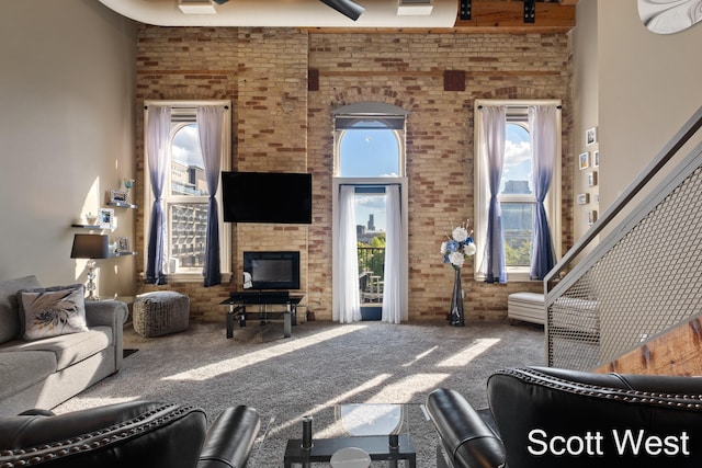 living room featuring carpet flooring, ceiling fan, a towering ceiling, and brick wall