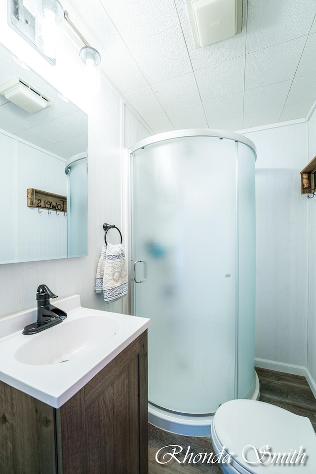 bathroom featuring vanity, hardwood / wood-style flooring, toilet, a shower with shower door, and wood walls
