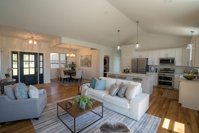 living room featuring sink, an inviting chandelier, high vaulted ceiling, stacked washer / dryer, and light hardwood / wood-style floors