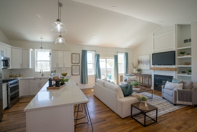 kitchen with appliances with stainless steel finishes, a wealth of natural light, vaulted ceiling, a center island, and white cabinetry