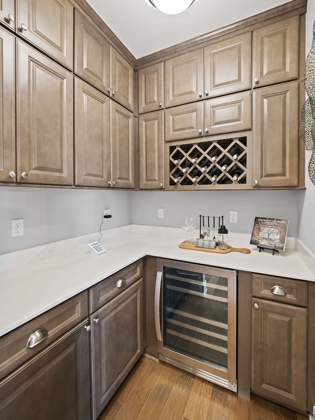 bar with dark brown cabinetry, beverage cooler, and light wood-type flooring