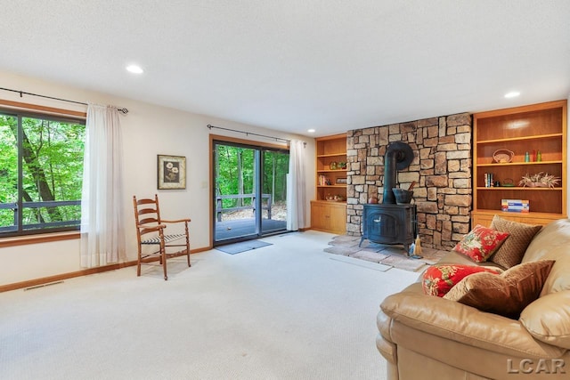 carpeted living room featuring a textured ceiling, a wood stove, plenty of natural light, and built in features