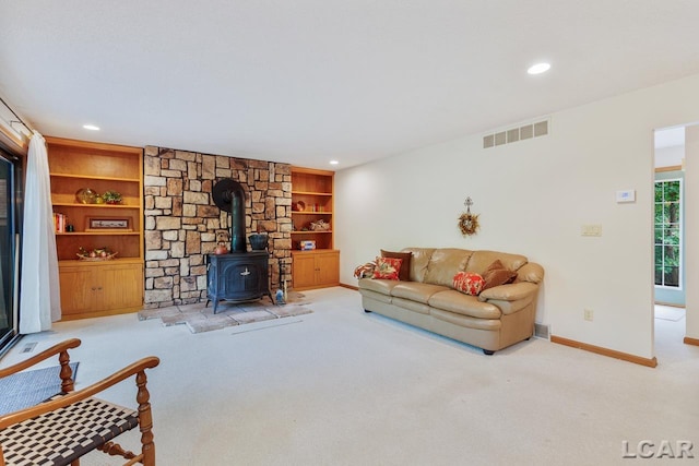 living room featuring a wood stove, built in shelves, and light colored carpet