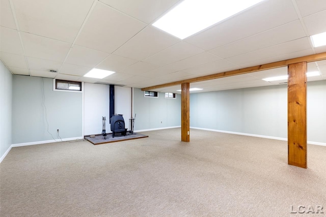 basement with carpet, a wood stove, and a drop ceiling