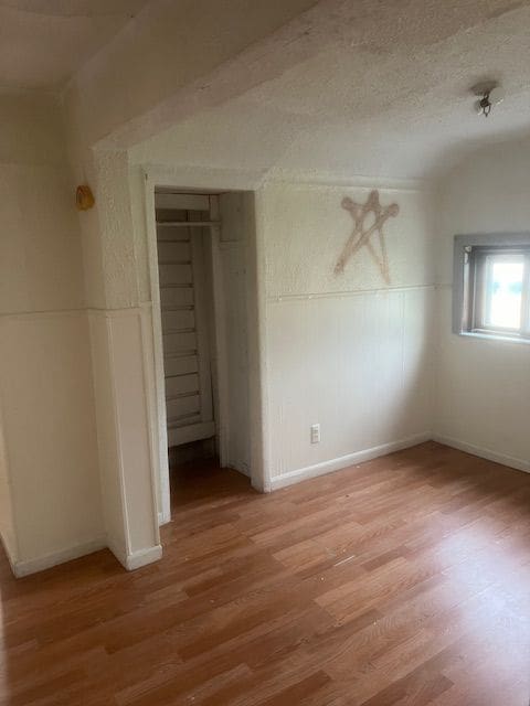 unfurnished bedroom featuring a textured ceiling, a closet, wood-type flooring, and vaulted ceiling