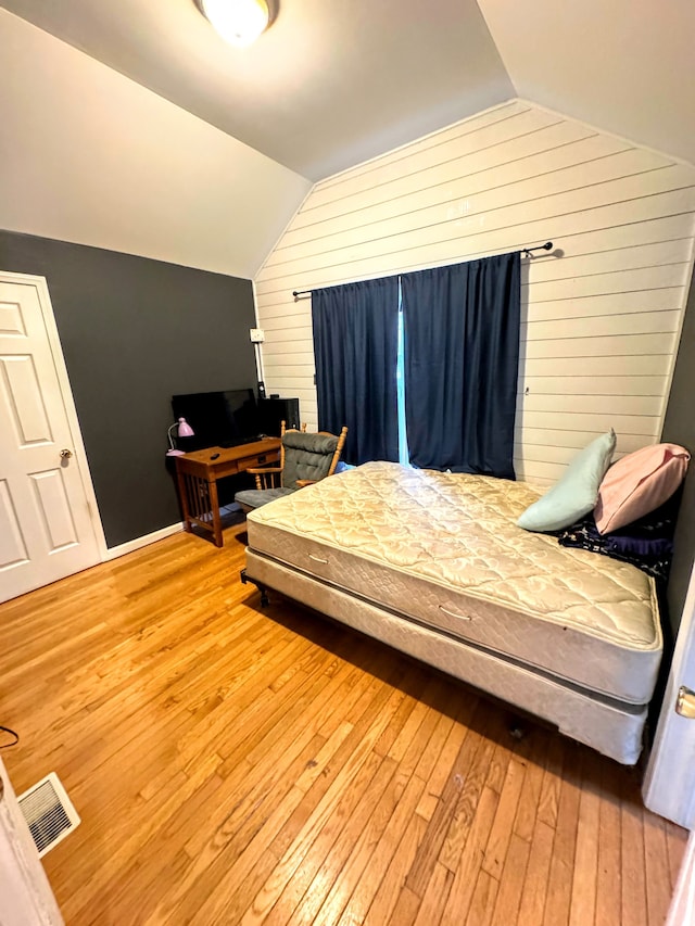 bedroom featuring wooden walls, hardwood / wood-style floors, and vaulted ceiling