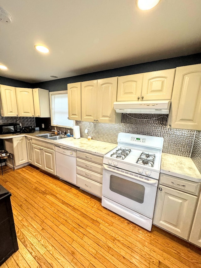 kitchen featuring light wood-type flooring, decorative backsplash, white appliances, and sink