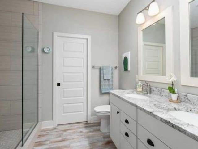 bathroom with hardwood / wood-style flooring, vanity, toilet, and tiled shower