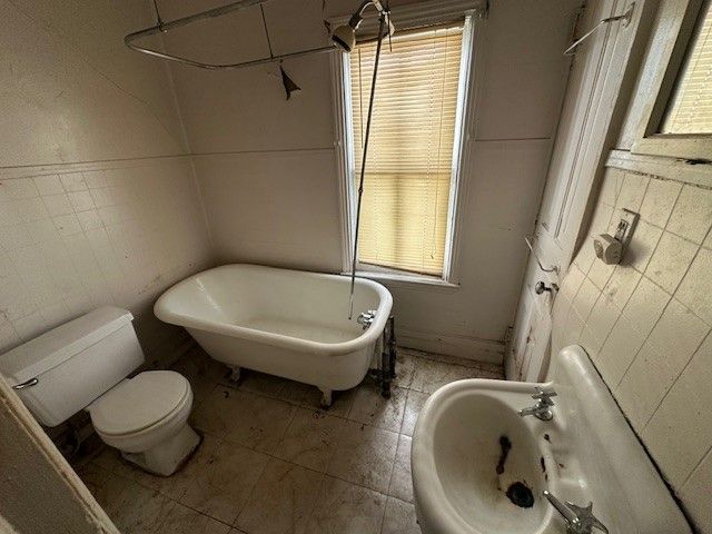 bathroom with a bathtub, tile patterned flooring, tile walls, and toilet