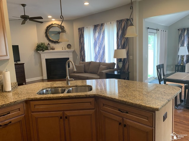 kitchen with ceiling fan, sink, light stone counters, decorative light fixtures, and hardwood / wood-style flooring