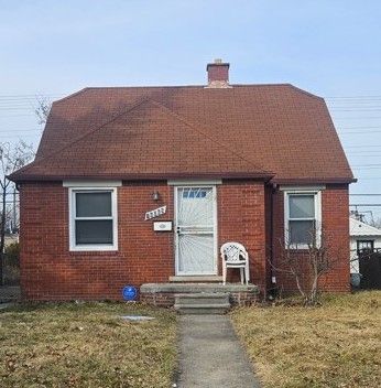 view of front of house featuring entry steps, brick siding, roof with shingles, a chimney, and a front yard