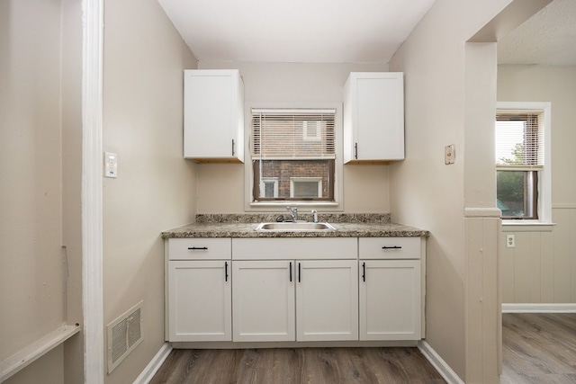 kitchen featuring white cabinetry, sink, wood-type flooring, and stone countertops