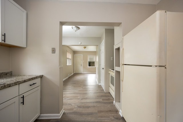 kitchen with dark stone countertops, white cabinets, light hardwood / wood-style floors, and white appliances