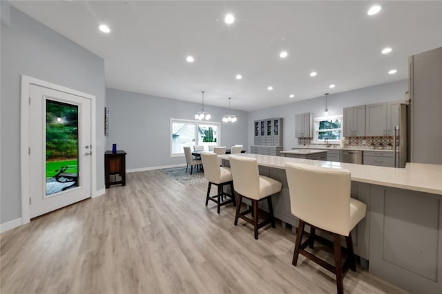 kitchen with a kitchen bar, light wood-type flooring, gray cabinetry, stainless steel appliances, and hanging light fixtures