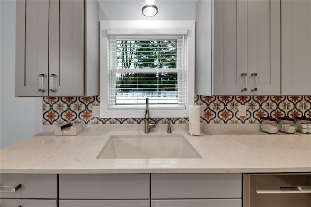 kitchen with backsplash, dishwasher, light stone counters, and sink