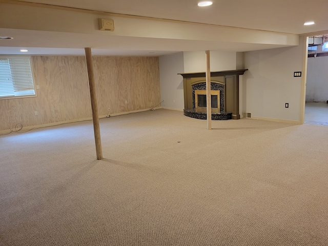 basement featuring light colored carpet, a wealth of natural light, and wood walls