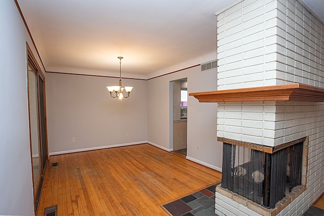 unfurnished living room with a brick fireplace, an inviting chandelier, ornamental molding, and hardwood / wood-style flooring