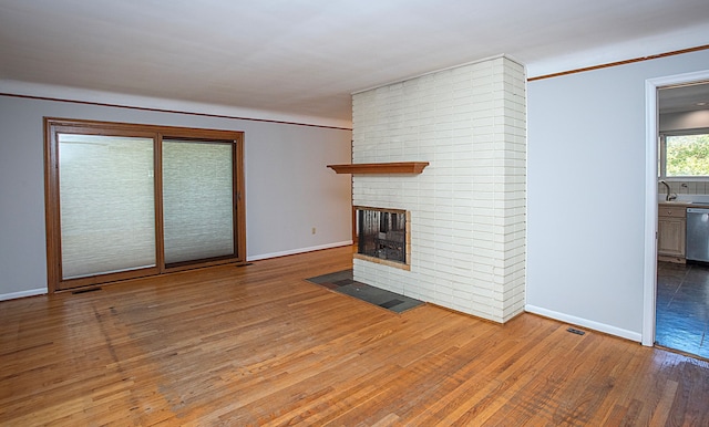 unfurnished living room featuring hardwood / wood-style flooring and a brick fireplace