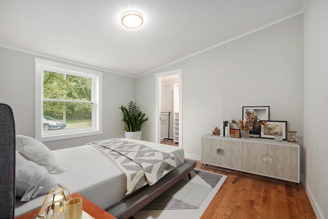 bedroom with a walk in closet, ornamental molding, a textured ceiling, dark wood-type flooring, and lofted ceiling