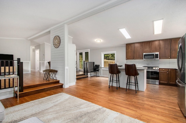 kitchen with a breakfast bar, appliances with stainless steel finishes, a center island, and light hardwood / wood-style flooring