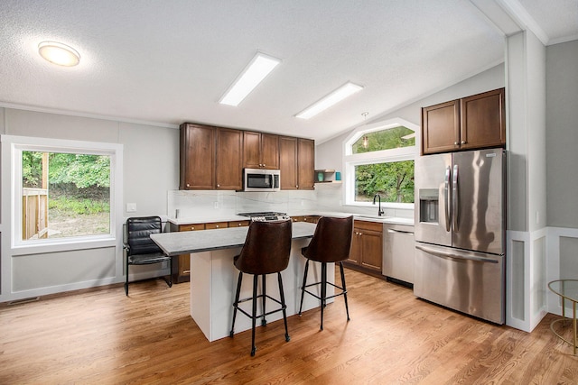 kitchen featuring vaulted ceiling, stainless steel appliances, a kitchen island, and a wealth of natural light