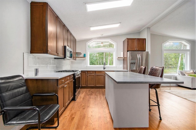 kitchen featuring a kitchen bar, lofted ceiling, appliances with stainless steel finishes, and light hardwood / wood-style flooring