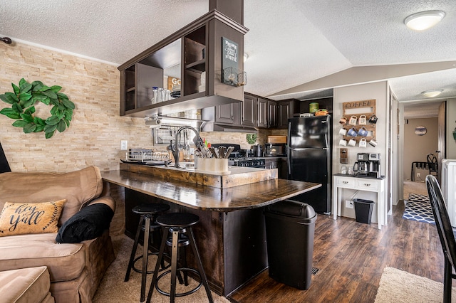 kitchen with lofted ceiling, dark wood-type flooring, black fridge, dark brown cabinetry, and kitchen peninsula