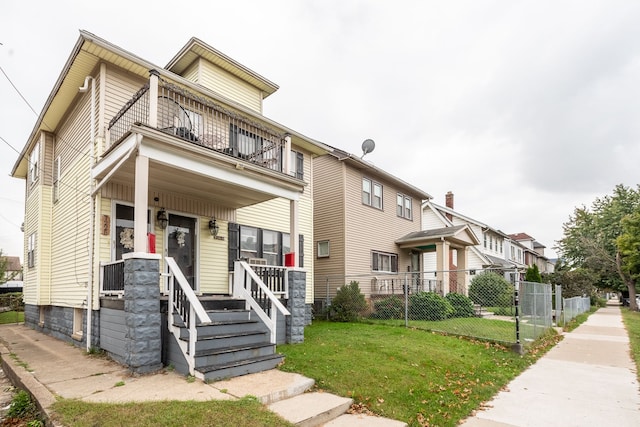 view of property with covered porch, a balcony, and a front lawn