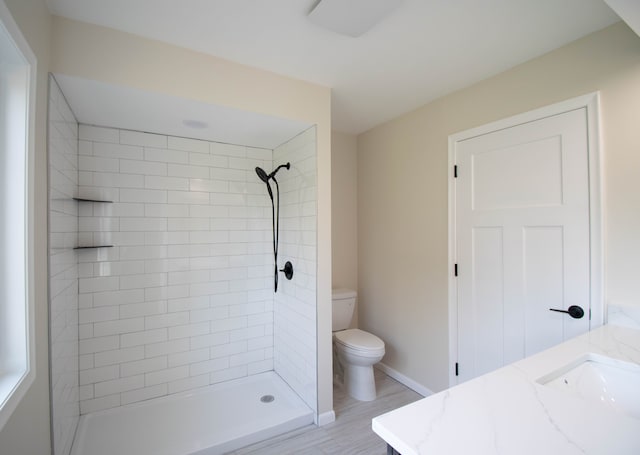 bathroom with hardwood / wood-style floors, vanity, toilet, and a tile shower