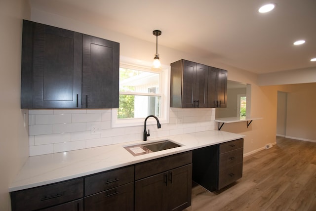 kitchen with hanging light fixtures, tasteful backsplash, sink, and light hardwood / wood-style floors