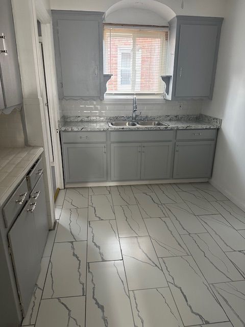 kitchen featuring gray cabinets, light stone counters, and sink