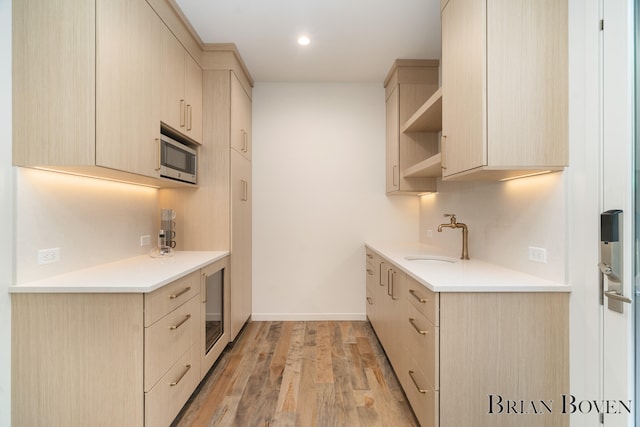 kitchen featuring light wood-type flooring, beverage cooler, sink, light brown cabinets, and stainless steel microwave