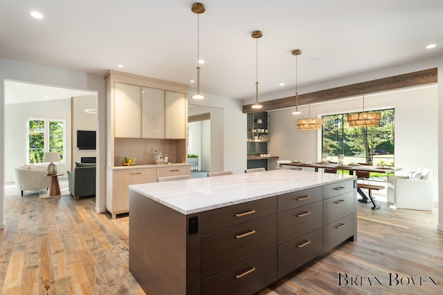 kitchen with backsplash, a kitchen island, light hardwood / wood-style floors, light stone counters, and dark brown cabinetry