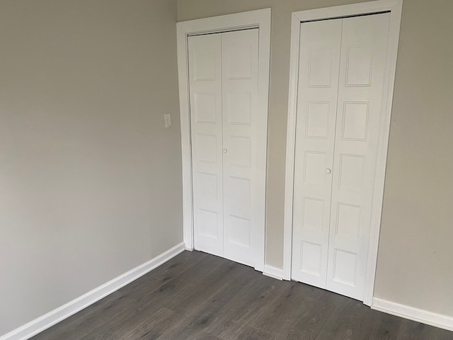 unfurnished bedroom featuring multiple closets and dark wood-type flooring