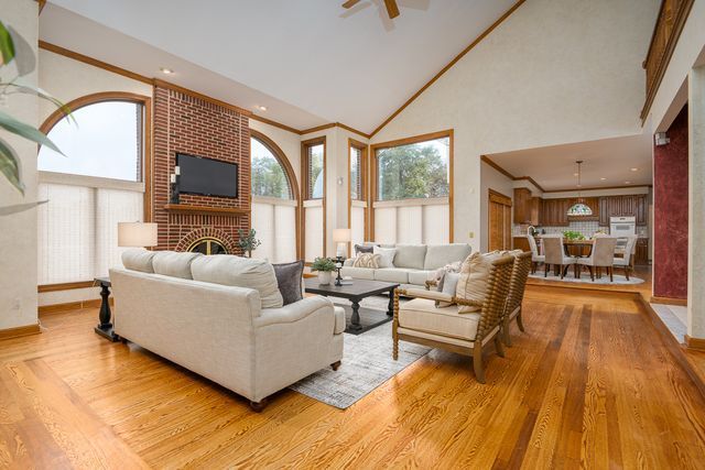 living room featuring a brick fireplace, light wood-type flooring, high vaulted ceiling, and crown molding