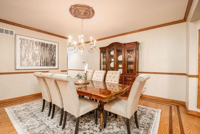 dining space featuring hardwood / wood-style flooring, crown molding, and an inviting chandelier