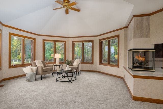 carpeted living room with a multi sided fireplace, ceiling fan, lofted ceiling, and ornamental molding