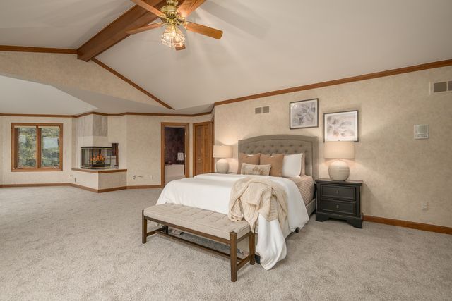 bedroom with light carpet, vaulted ceiling with beams, ceiling fan, and crown molding