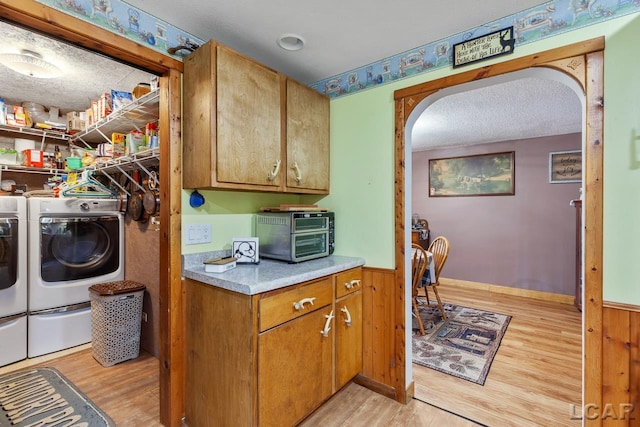 clothes washing area featuring a textured ceiling, light hardwood / wood-style flooring, wooden walls, and washing machine and clothes dryer