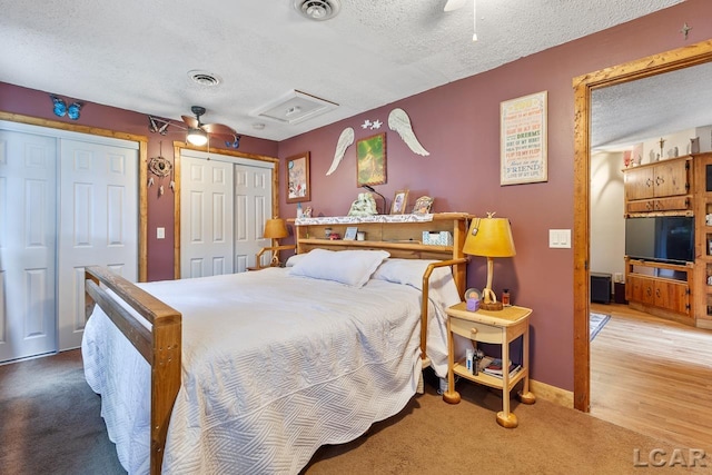 bedroom with multiple closets, ceiling fan, hardwood / wood-style floors, and a textured ceiling