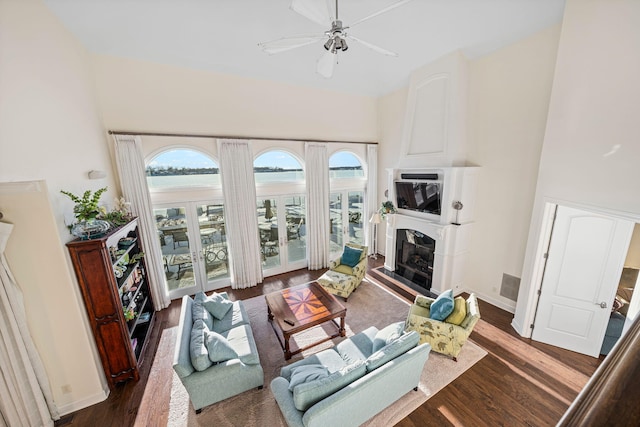 living room featuring dark wood finished floors, plenty of natural light, a fireplace with raised hearth, and ceiling fan