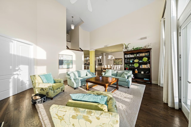 living room with ceiling fan with notable chandelier, decorative columns, wood finished floors, and a towering ceiling