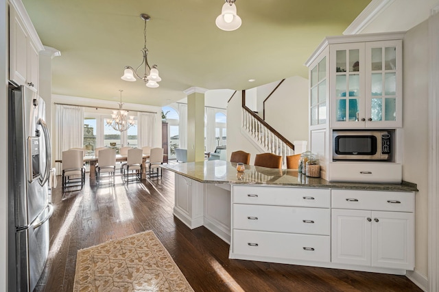 kitchen with dark stone countertops, dark wood-style floors, stainless steel appliances, white cabinetry, and a chandelier