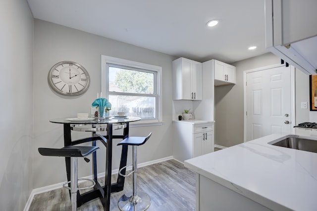 kitchen with sink, light hardwood / wood-style flooring, white cabinetry, and light stone counters